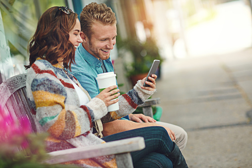 Shot of a happy young couple using a smartphone together while spending the day downtown