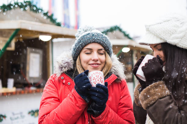 istock Women drinking hot drinks at Christmas market while snowing 645990584