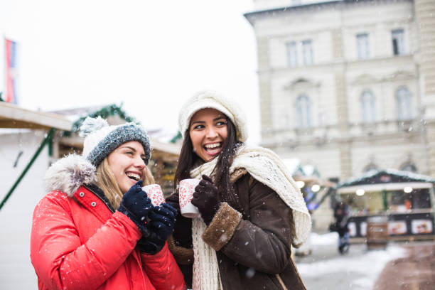 Friends at Christmas market Two young female friends drinking hot chocolate at Christmas market while snowing. punch drink stock pictures, royalty-free photos & images