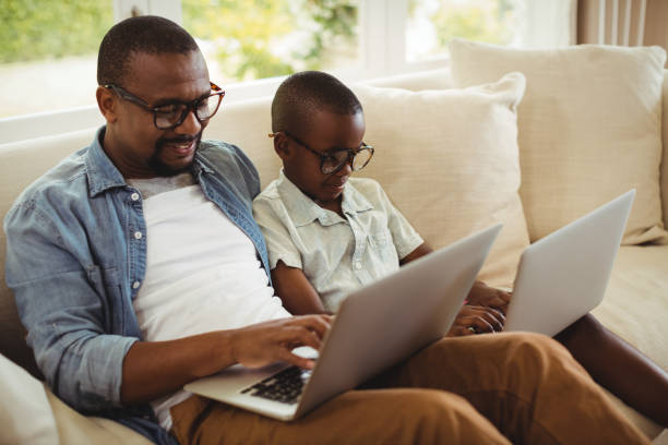 istock Father and son sitting on sofa and using laptop 646001728
