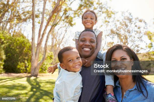 Family Carrying Children On Shoulders As They Walk In Park Stock Photo - Download Image Now