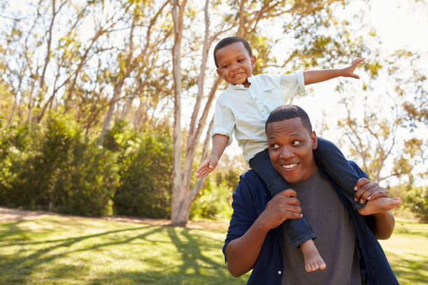 istock Father Carrying Son On Shoulders As They Walk In Park 646011752