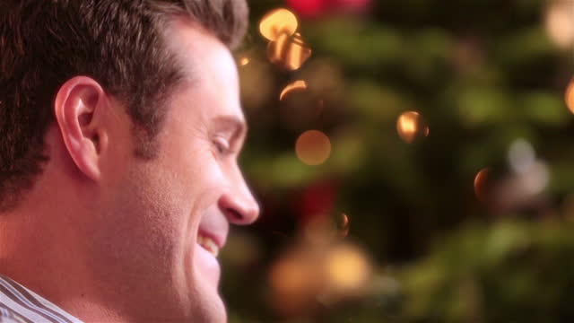 Father laughs as son tears into present in front of Christmas tree