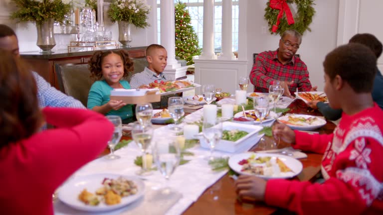 Family pass plates around table for Christmas dinner, cute young girl smells sweet potatoes hungrily as father serves them (dolly-shot)