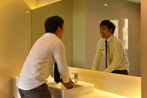 An Asian man washing hands in bathroom, looking at luxury restroom, person