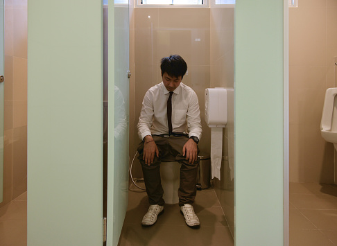 An Asian business man pooping in bathroom, diarrhea