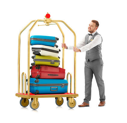 a luggage trolley fully laden with luggage  being pushed along by a hotel porter