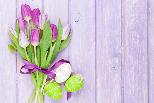 Purple tulip bouquet and easter eggs on wooden table with copy space