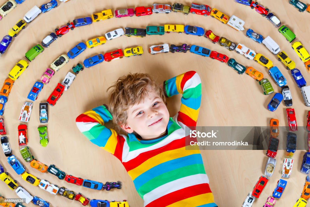 Cute little blond kid boy playing with lots toy cars Cute little blond kid boy playing with lots of toy cars indoor. Child wearing colorful shirt. Happy preschooler having fun at home or nursery. Big collection of different vehicles. Happiness game Child Stock Photo