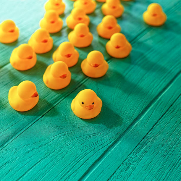 istock Group of blind yellow rubber ducks following behind one seeing leading duck in front, on a turquoise coloured wooden background. 646048196