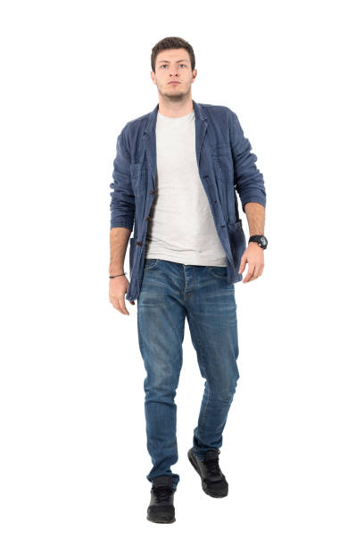 Confident man in denim shirt and jeans walking towards camera Young confident man in denim unbuttoned shirt and jeans walking towards camera. Full body length portrait isolated over white background. full body isolated stock pictures, royalty-free photos & images