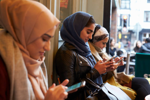 Group Of British Muslim Women Texting Outside Coffee Shop Group Of British Muslim Women Texting Outside Coffee Shop pakistani ethnicity stock pictures, royalty-free photos & images