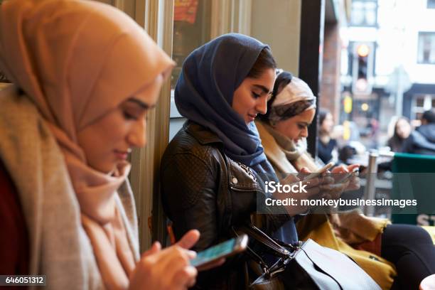 Group Of British Muslim Women Texting Outside Coffee Shop Stock Photo - Download Image Now