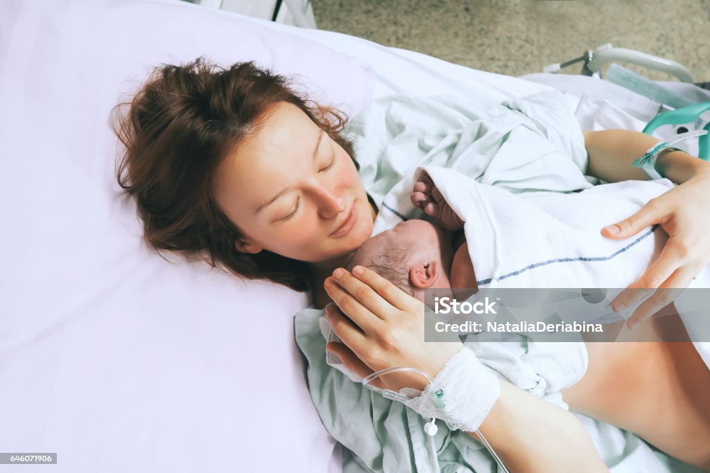 Mother holding her newborn baby child after labor in a hospital. Mother holding her newborn baby child after labor in a hospital. Mother giving birth to a baby boy. Parent and infant first moments of bonding. Childbirth Stock Photo