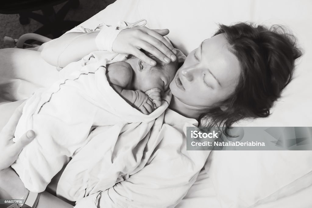 Mother holding her newborn baby child after labor in a hospital. Mother holding her newborn baby child after labor in a hospital. Mother giving birth to a baby boy. Black and white photo. Labor - Childbirth Stock Photo