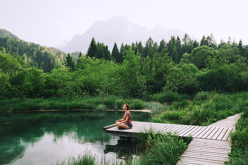 Young woman doing yoga and meditating in lotus position on the background of nature. Concept of Meditation, Relaxation and Healthy Life. Slovenia, Europe.