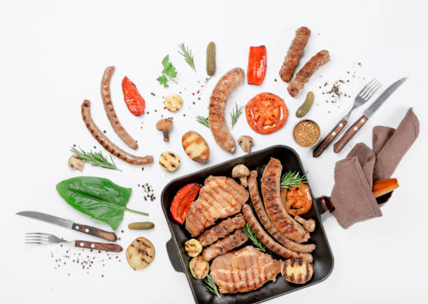istock Steak and different sausages and grilled vegetables on white background in cast iron grill pan 646085562