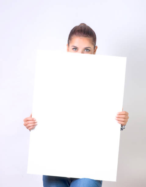 donna sbirciando oltre bordo di cartellone di carta vuota vuota - advertisement advertise businesswoman peeking foto e immagini stock
