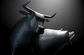 Two metal castings depicting a stylized bull alongside a bear in dramatic light representing  financial market trends