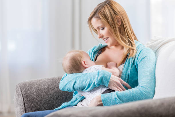 Mom breastfeeds daughter at home Beautiful mom breastfeeds her daughter at home. They are sitting on the sofa. suckling stock pictures, royalty-free photos & images