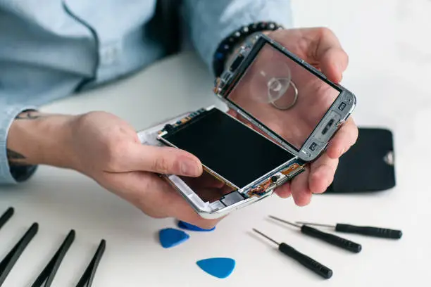 Repairman disassembling smartphone close-up. Male hands holding opened mobile phone for diagnostics, repair tools on workplace. Electronic fixing, modern technology, business concept