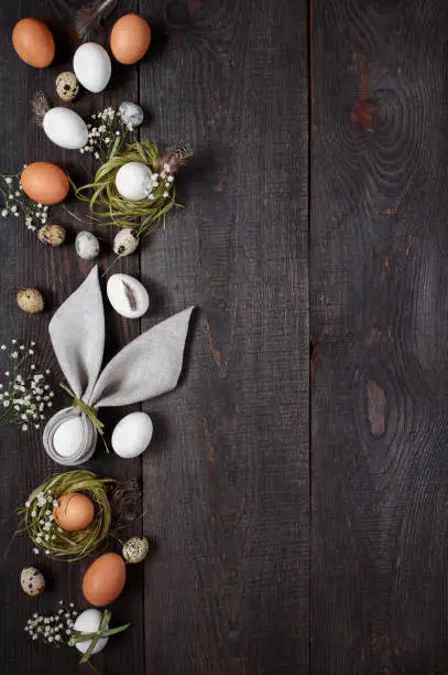 Dark-brown wooden background with eggs, nests, flowers, feathers and nupkin
