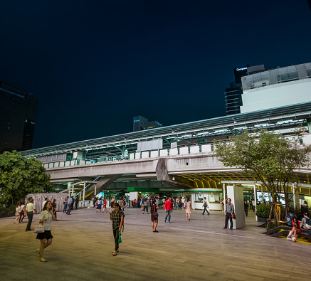 Bangkok, Thailand - September 22, 2016: A view of the BTS elevated railway line at night in the center of the Thai capital. With pedestrians walking in the foreground.
