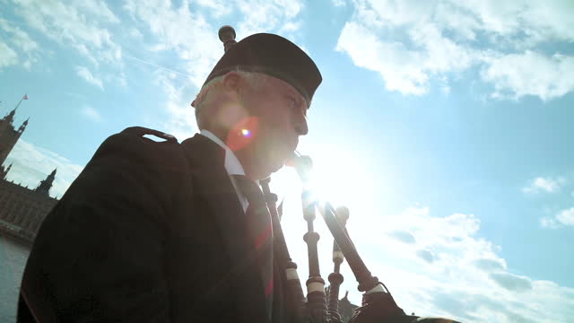 Traditional bagpipe player performs on Westminster Bridge with lens flare.