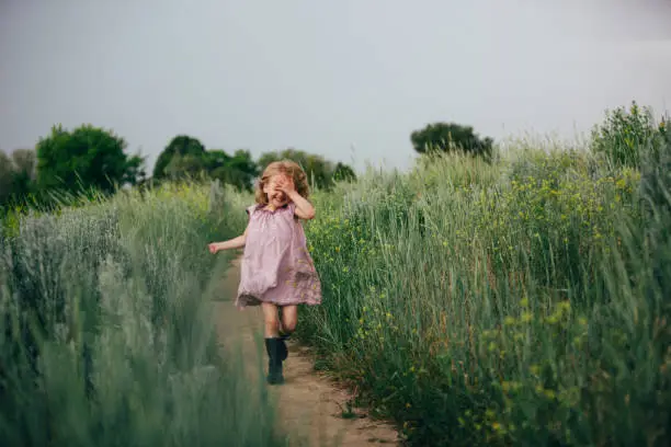 Photo of Toddler girl running on a path in a field of green tall grass