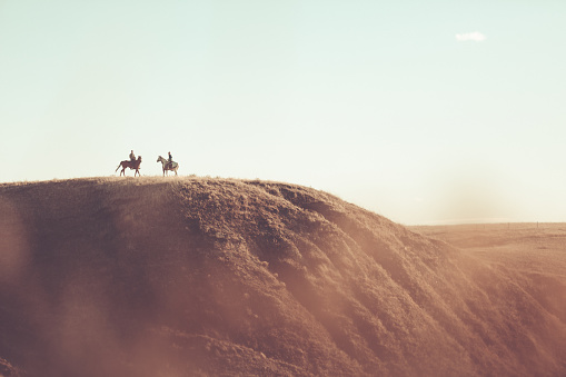 A man and woman sitting on horseback on top of a grassy hill on Montana prairie.