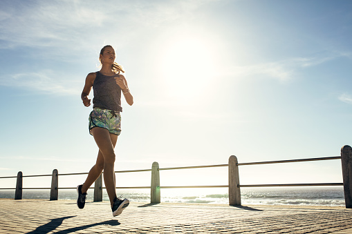 Outdoor shot of fitness young woman jogging along the beach. Female runner running outdoors on seaside promenade.