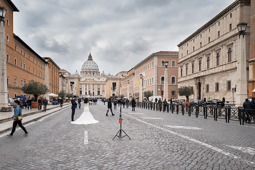Rome, Italy - February 23, 2017: Tourists visiting the Vatican City in Rome. A couple taking a break from their wedding pictures, during February in front of the St. Peter's Basilica on the road leading to Piazza San Pietro.
