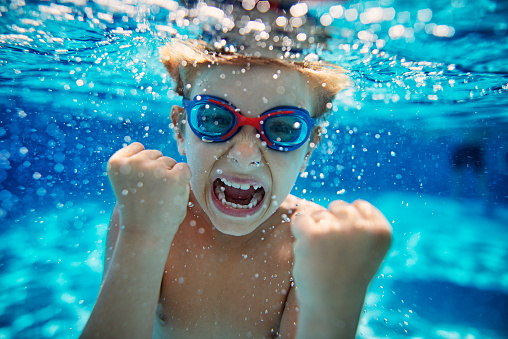 Little boy aged 6 swimming underwater. The boy is screaming at the camera with strong emotion.