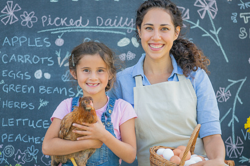 A mother and daughter are selling eggs at the local farmers market. They are smiling and looking at the camera.