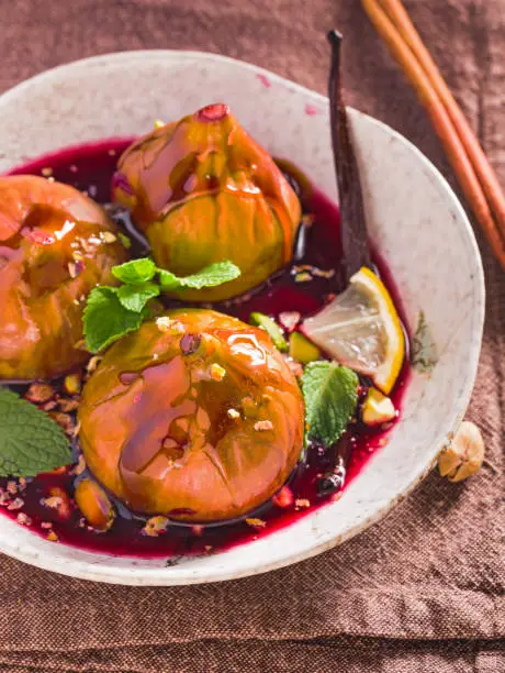 Poached figs in red wine with honey, pistachios and mint on table. Closeup