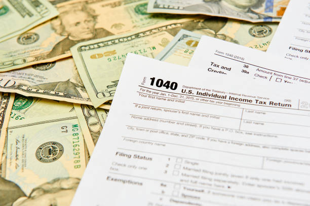1040 Individual Tax Return form on top of a table full of paper money. 1040 Individual Tax Return form on top of a table full of paper money. tax season photos stock pictures, royalty-free photos & images