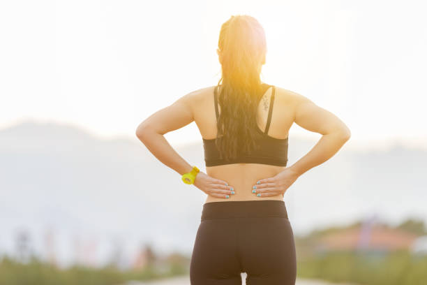 atlética jovem mulher a fricção músculos da parte inferior das costas depois de jogging - low back imagens e fotografias de stock