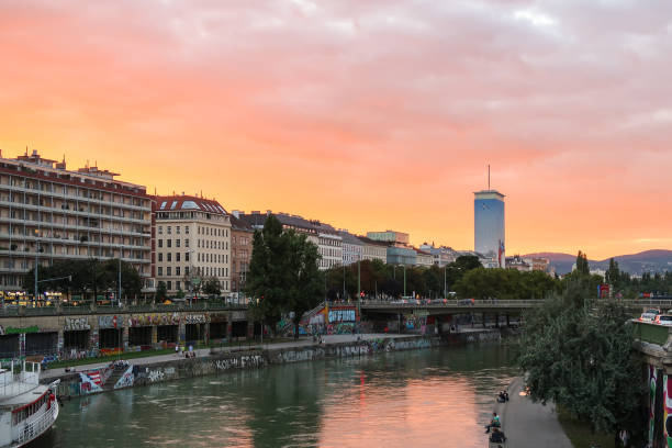 A view along the Danube Canal in Vienna at sunset in the summer. People can be seen sitting outside.