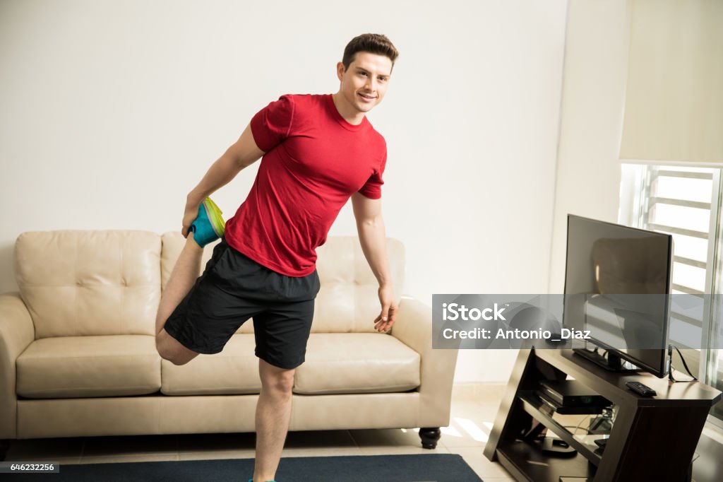 Athletic man stretching up his legs at home Portrait of a fit and athletic guy stretching his legs and warming up before exercising at home Active Lifestyle Stock Photo