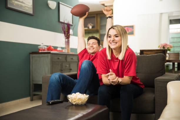 Couple celebrating a touchdown Cute couple looking excited and happy after their favorite football team scored a touchdown excited football fan cheering for his team on tv stock pictures, royalty-free photos & images