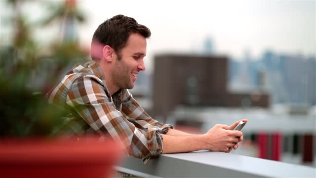 Hip young man on Brooklyn rooftop laughs at funny text-message (dolly-shot)
