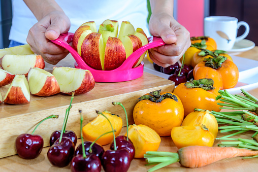 Woman's hands cutting apple with cutlery equipment, variety fruits in colorful modern kitchen / healthy lifestyle conceptual