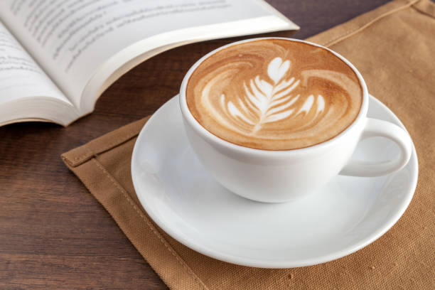 istock Coffee cup of rosetta latte art with a book beside 646315520