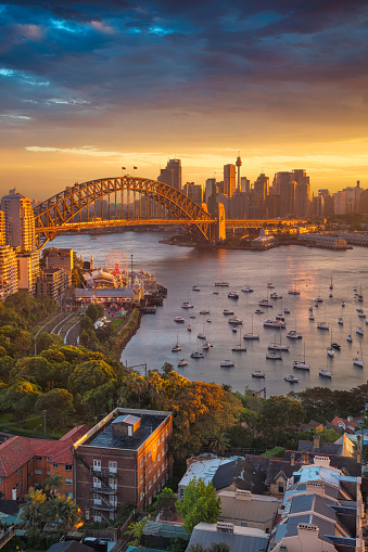 Cityscape image of Sydney, Australia with Harbour Bridge and Sydney skyline during sunset.