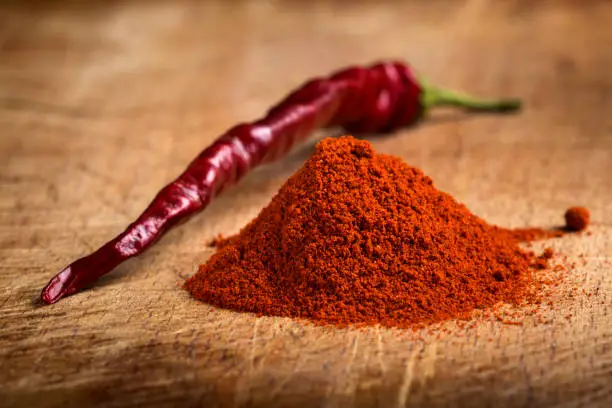Photo of Red hot paprika powder heap and one dried chilli