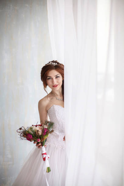 istock Happy young bride with wedding bouquet near window, vertical photo 646387876