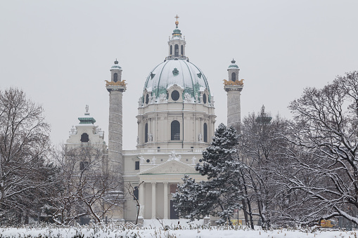 The front of Karlskirche in central Vienna during the winter. Lots of snow and trees can be seen.