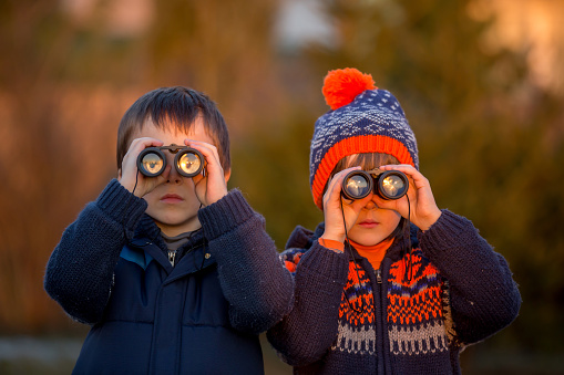 Two little children, boys, exploring nature with binoculars, looking at sunset