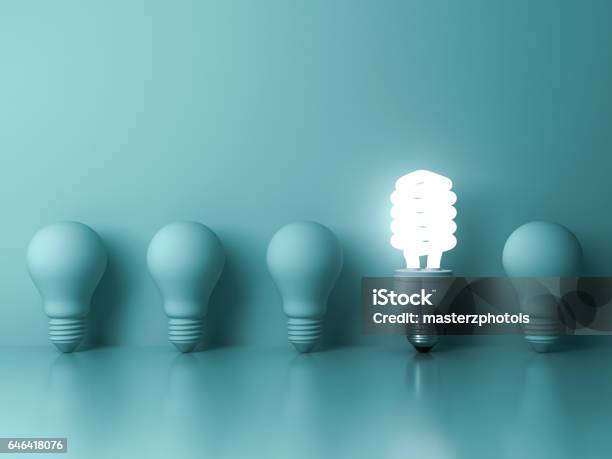 Eco Energy Saving Light Bulb One Glowing Compact Fluorescent Lightbulb Standing Out From Unlit Incandescent Bulbs Reflection On Green Background Stock Photo - Download Image Now