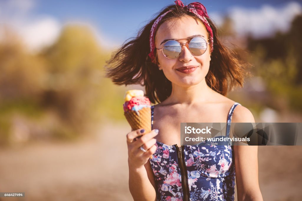 Young woman eating ice cream on the beach Young brunette woman in boho style eating ice cream at the beach Ice Cream Stock Photo